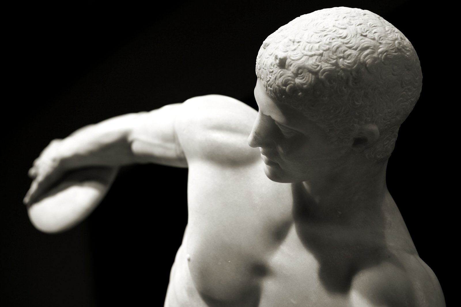 Marmor-Skulptur eines nackten Athleten, der zum Diskuswurf ausholt, Koerper in Spannung